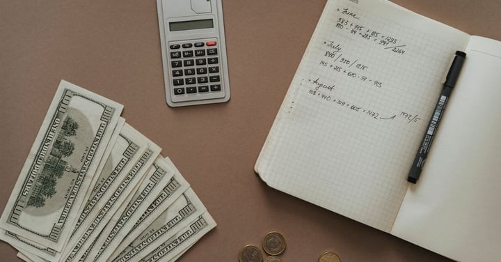Calculator, cash and a notebook of handwritten budget figures on a desk, as when working out program costs