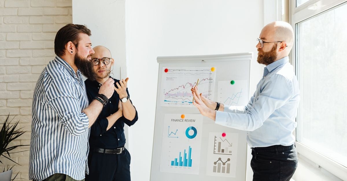 Three colleagues discussing charts pinned to a flip board while weighing options together
