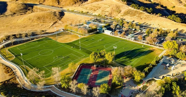 Aerial view of a park sports complex with a soccer field and tennis courts
