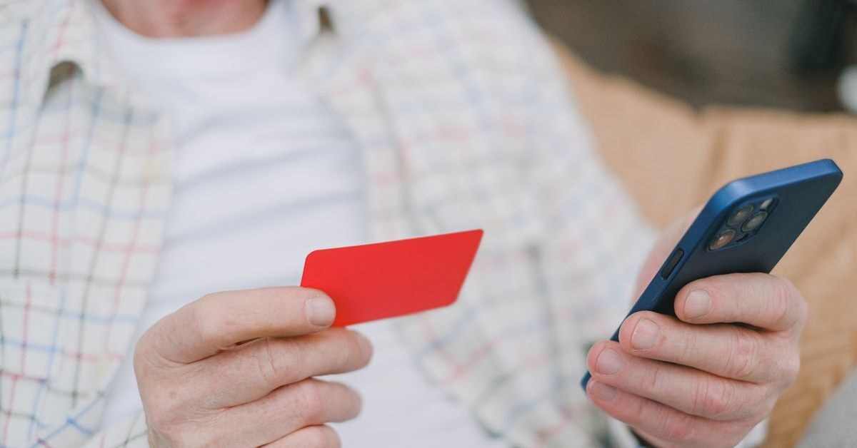 Adult holding a plain payment card in one hand and a smartphone in the other, ready to pay online