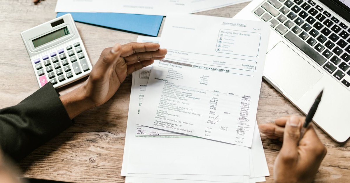 Hands reviewing financial documents beside a calculator and laptop