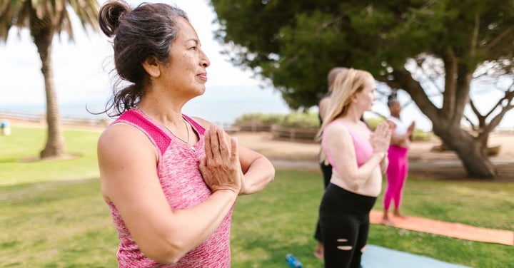 Older adults doing a guided outdoor yoga class on a park lawn under trees