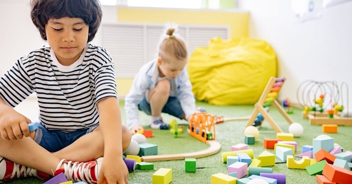 Two young children playing with blocks and toys in a bright classroom