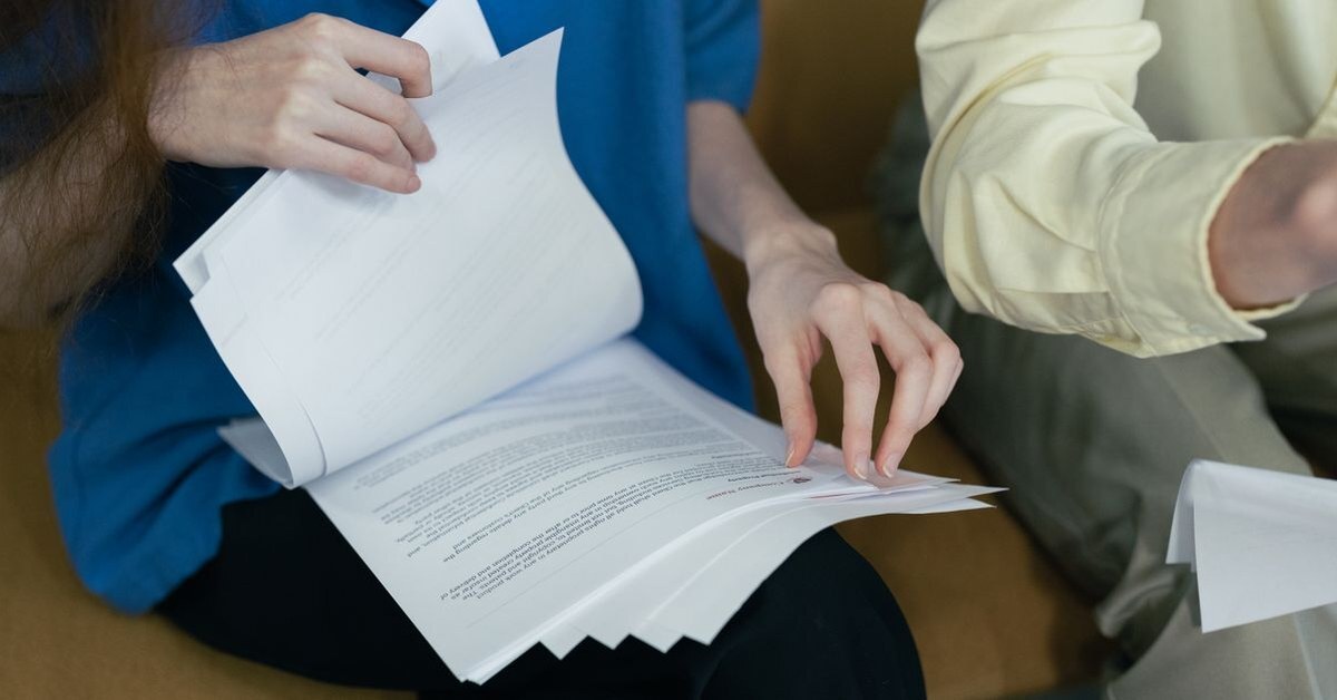 Two people paging through a thick stack of printed contract pages to check the terms