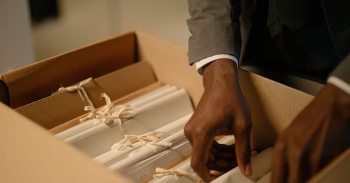 Hands sorting through a box of filed paper records, the legacy data a department must clean up before software go-live