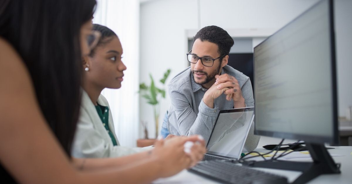 Three colleagues gathered at a desktop computer, one leaning in to watch a software walkthrough