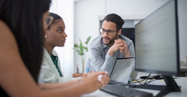 Three colleagues gathered at a desktop computer, one leaning in to watch a software walkthrough