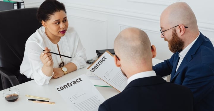 Three professionals seated at a table reviewing printed contract documents together