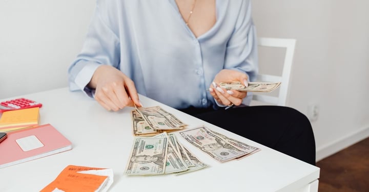 Staff member sorting and counting a spread of dollar bills at a desk beside a calculator and paper receipts