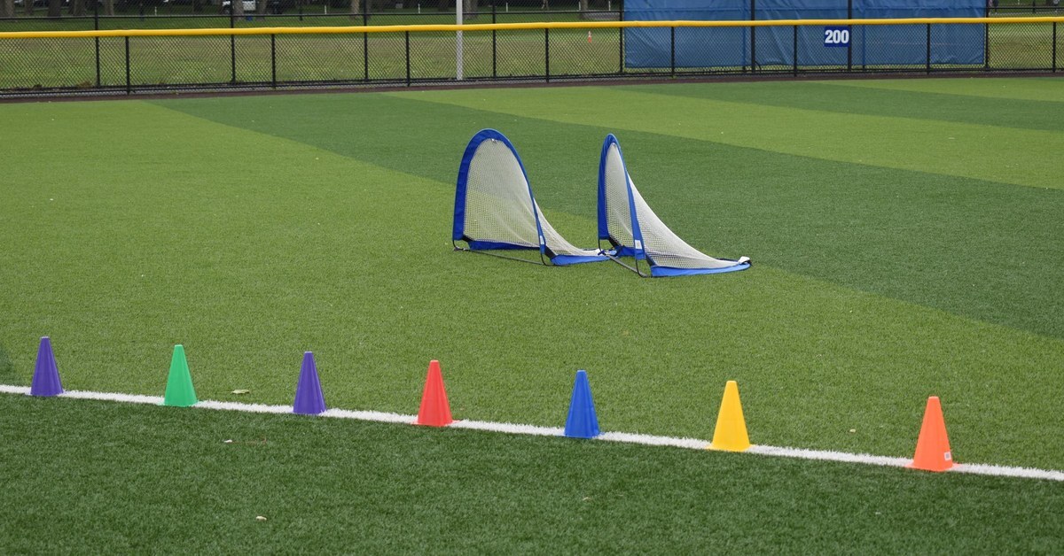 Colored training cones lined up along the sideline with two pop-up goals set out on a turf field before practice
