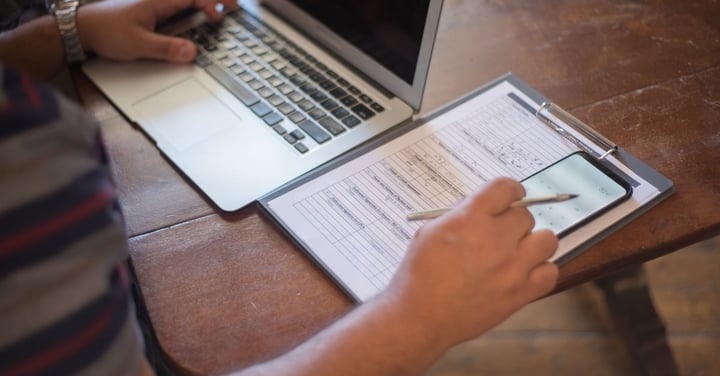 Paper registration form on a clipboard beside an open laptop and phone, showing a league moving sign-ups from paper to online