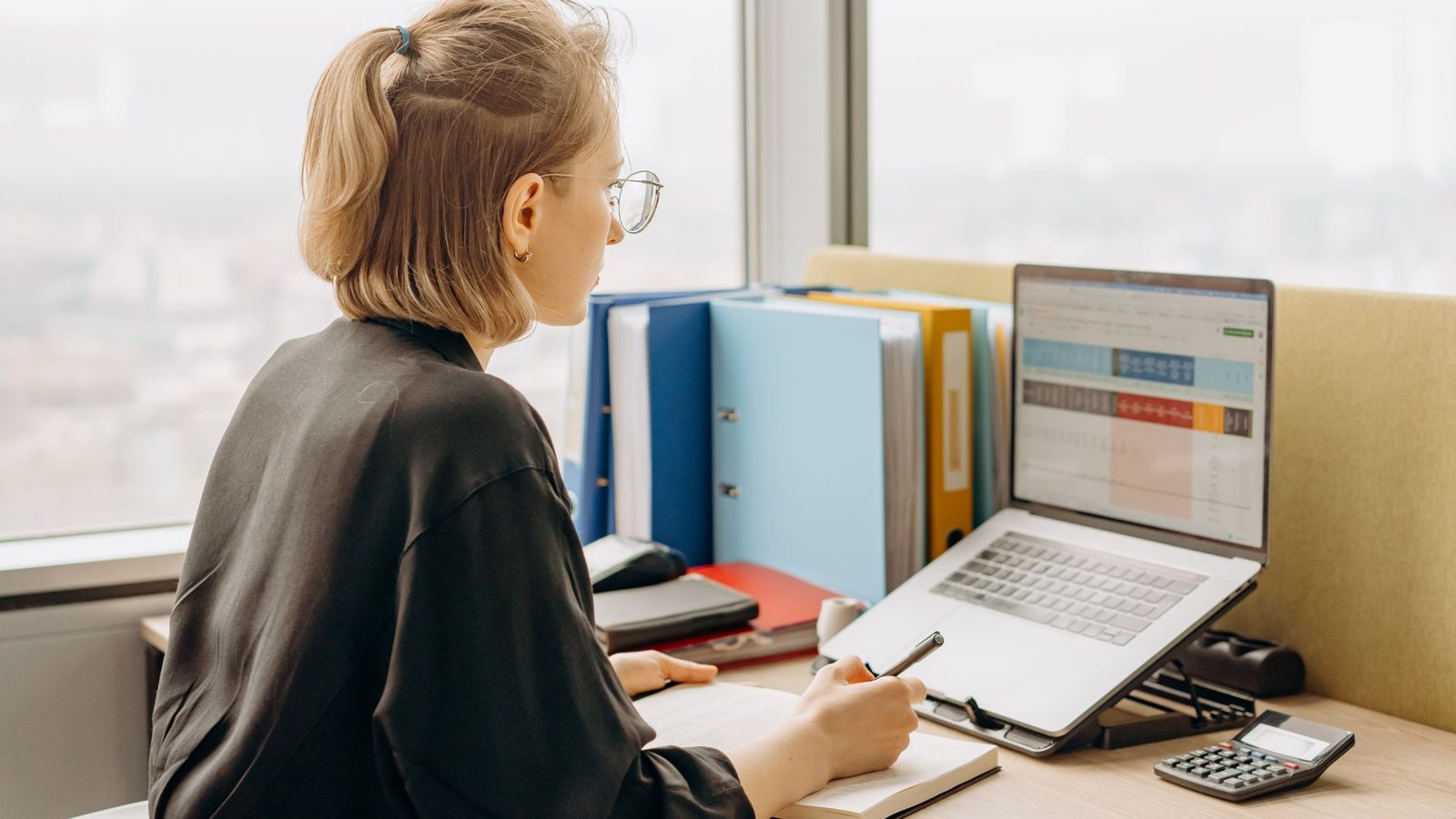 Staff member working in a spreadsheet on a laptop beside binders and a calculator